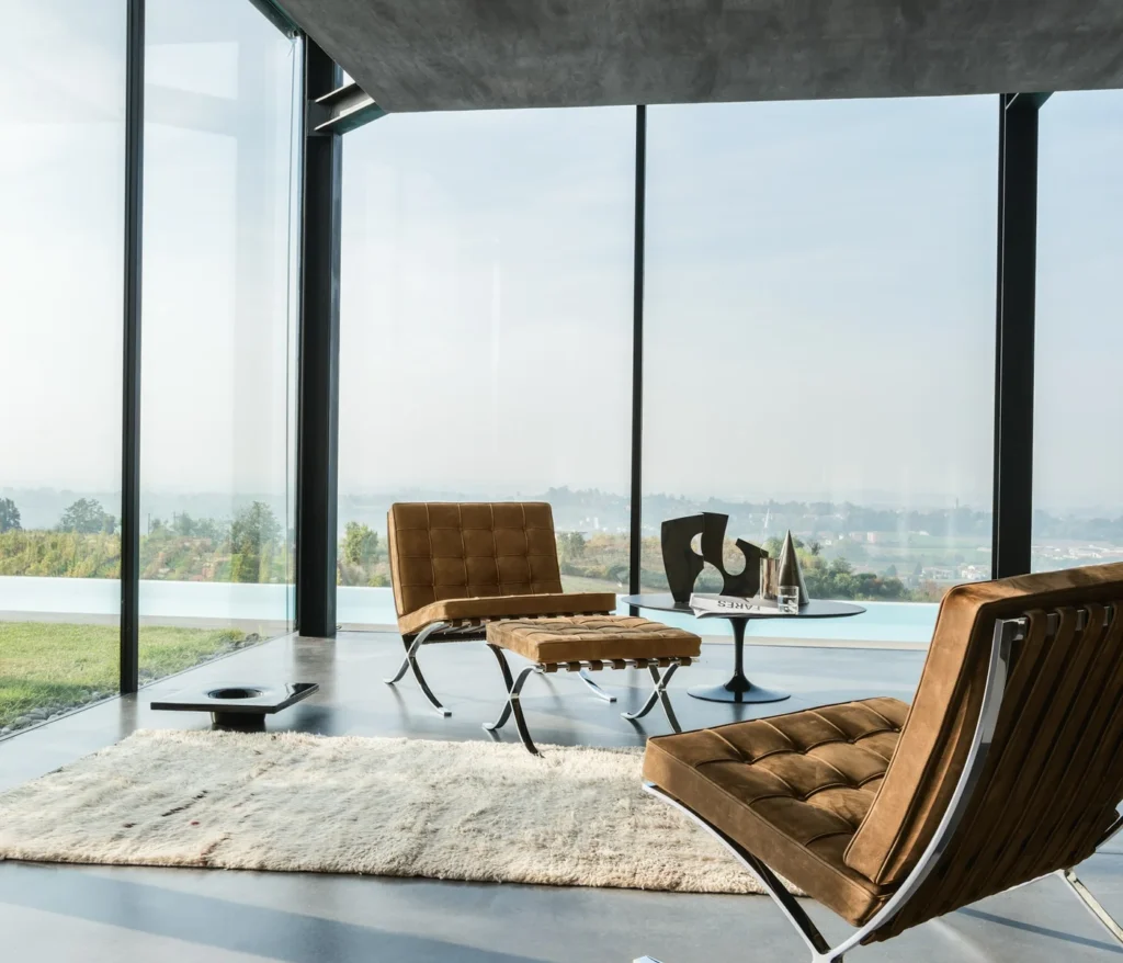 Zwei braune Knoll Barcelona Sessel vor einer Glasfront mit Blick über eine Landschaft