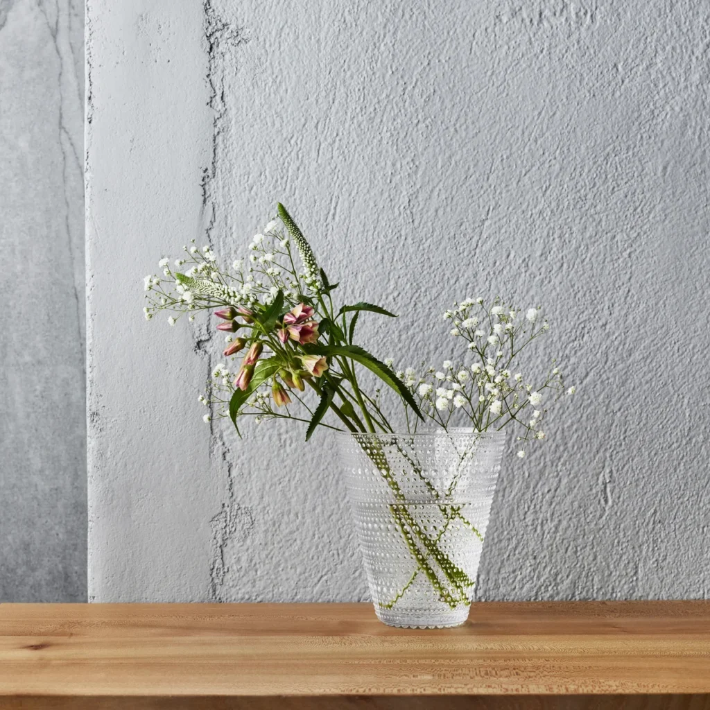 Iittala Kastehelmi Vase aus Klarglas mit weißen Blüten vor einer hellen Wand