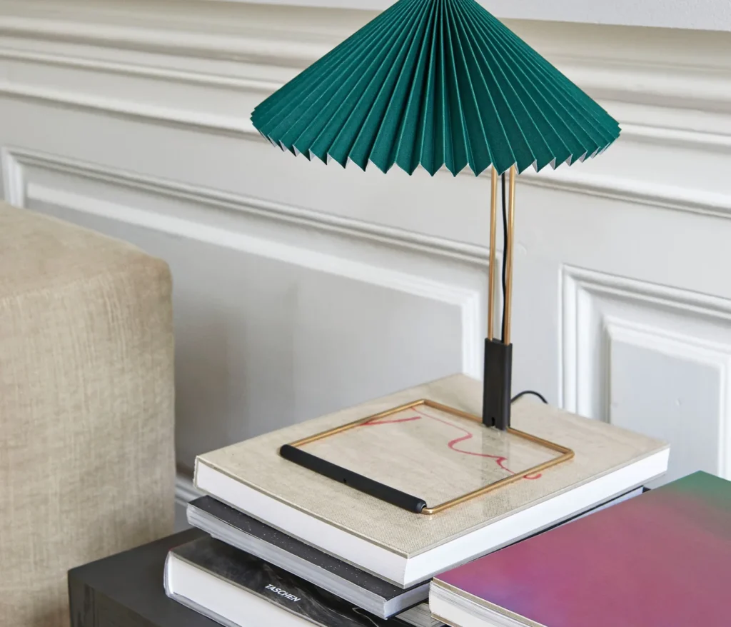 HAY Matin Tischleuchte mit grünem Plisseeschirm auf einem Bücherstapel