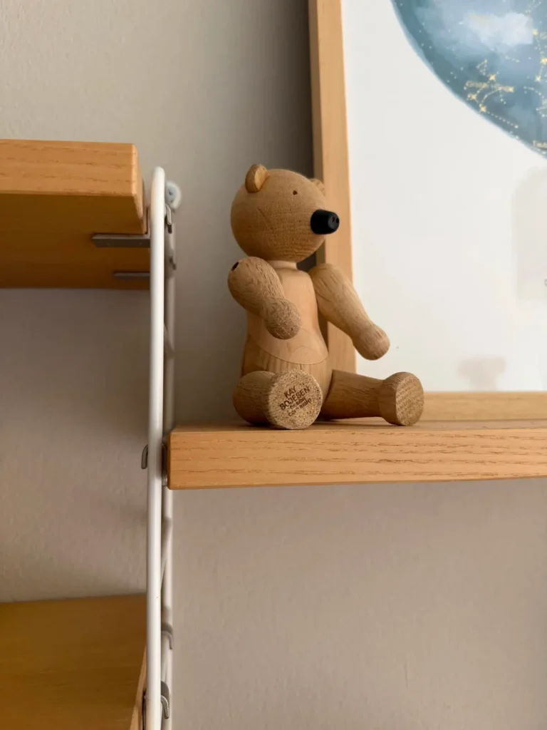 Eckdetail eines String Regals mit Eichenboden und weißer Metallleiter, darauf eine kleine Holzfigur als Dekoration vor heller Wand