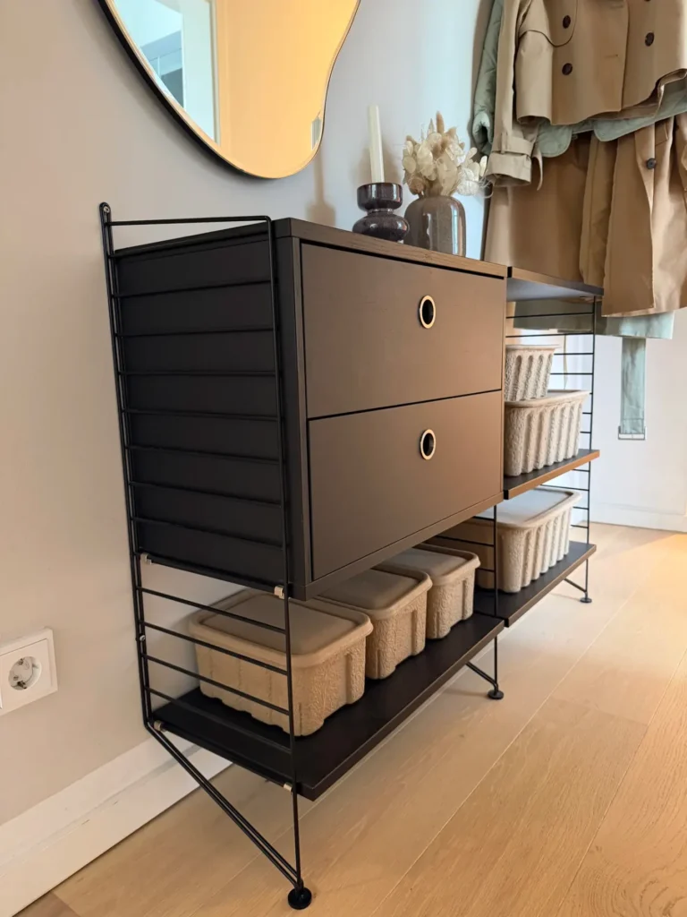 Freistehendes String Regal als Flurgarderobe mit schwarzem Metallrahmen, Eichenböden, schwarzen Kästen und geflochtenen Aufbewahrungsboxen vor einem Spiegel