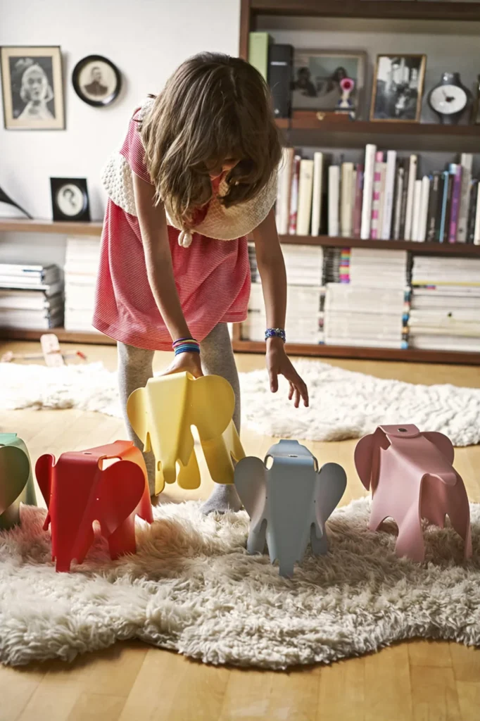Mädchen spielt auf einem hellen Teppich mit mehreren kleinen Vitra Eames Elephants in Rot, Gelb, Grau und Rosa